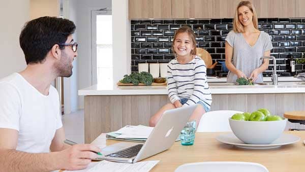 Happy family while mother working in kitchen, father on laptop and small happily sitting on table