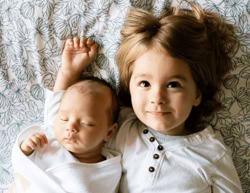 Cute small sister laying on bed with her baby brother