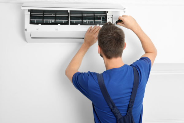 Male technician repairing air conditioner indoors.